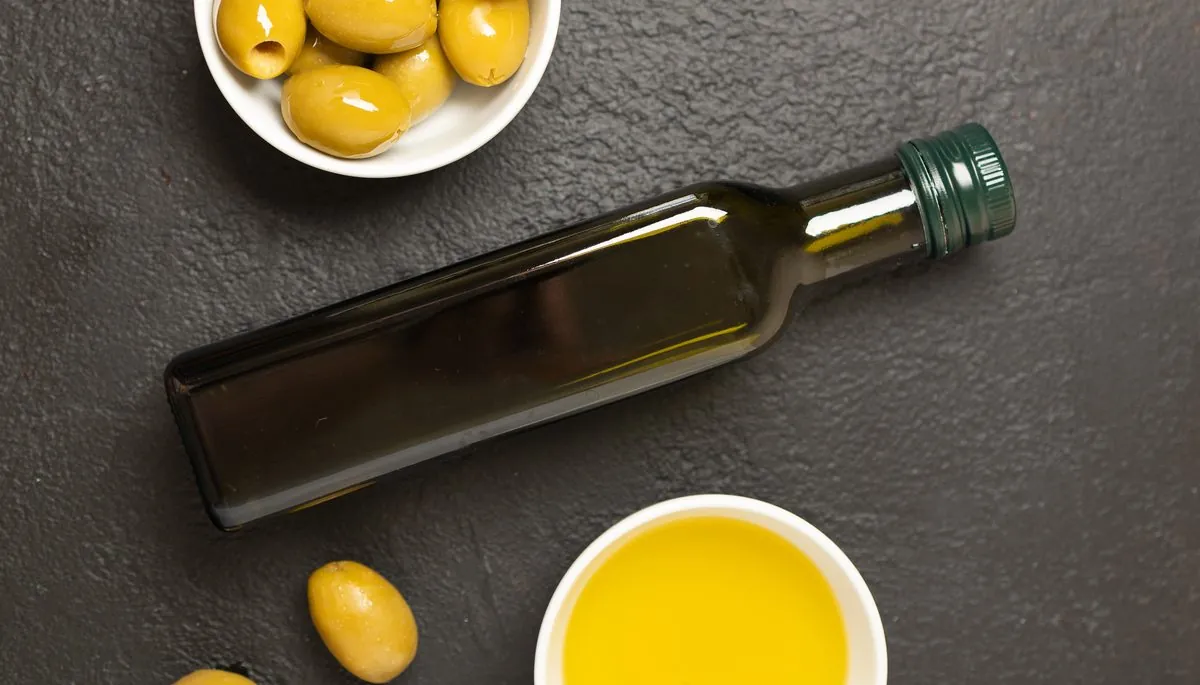Koyu zeminde zeytinyağı şişesi, zeytin kâsesi ve yağ tabağı